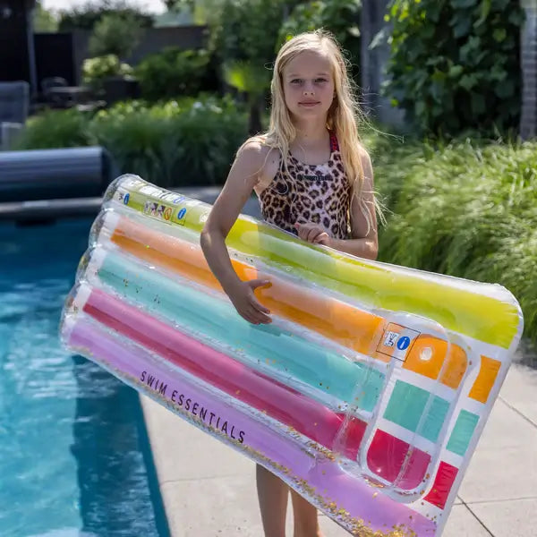 luchtmatras meisje kind tiener swim essentials regenboog glitter rainbow opblaasbaar luchtbed waterspeelgoed sfeerfoto meisje met luchtmatras hoofdkussen aan zwembad